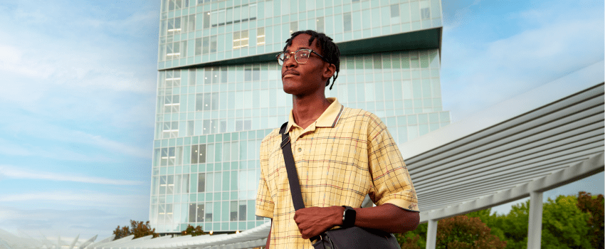 A student standing outside of the Dubois Center on a sunny day.